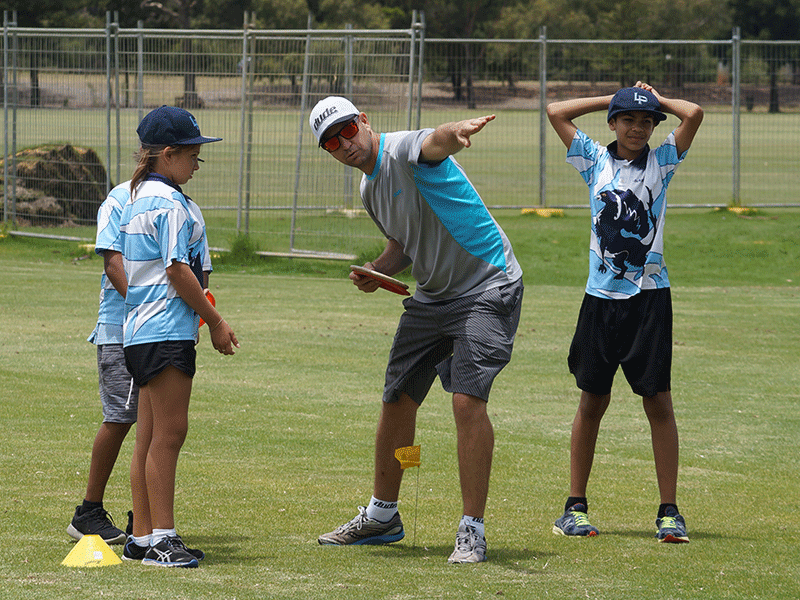 an image of a man teaching three children on how to play frisbee