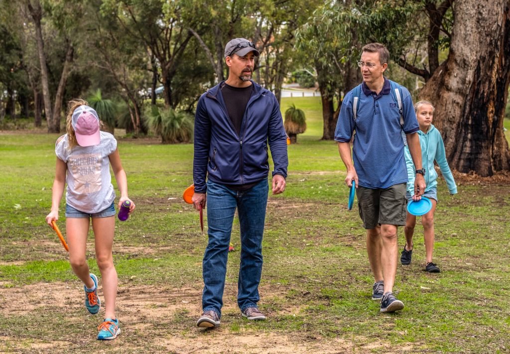 An image of men and kids walking in a disc golf park