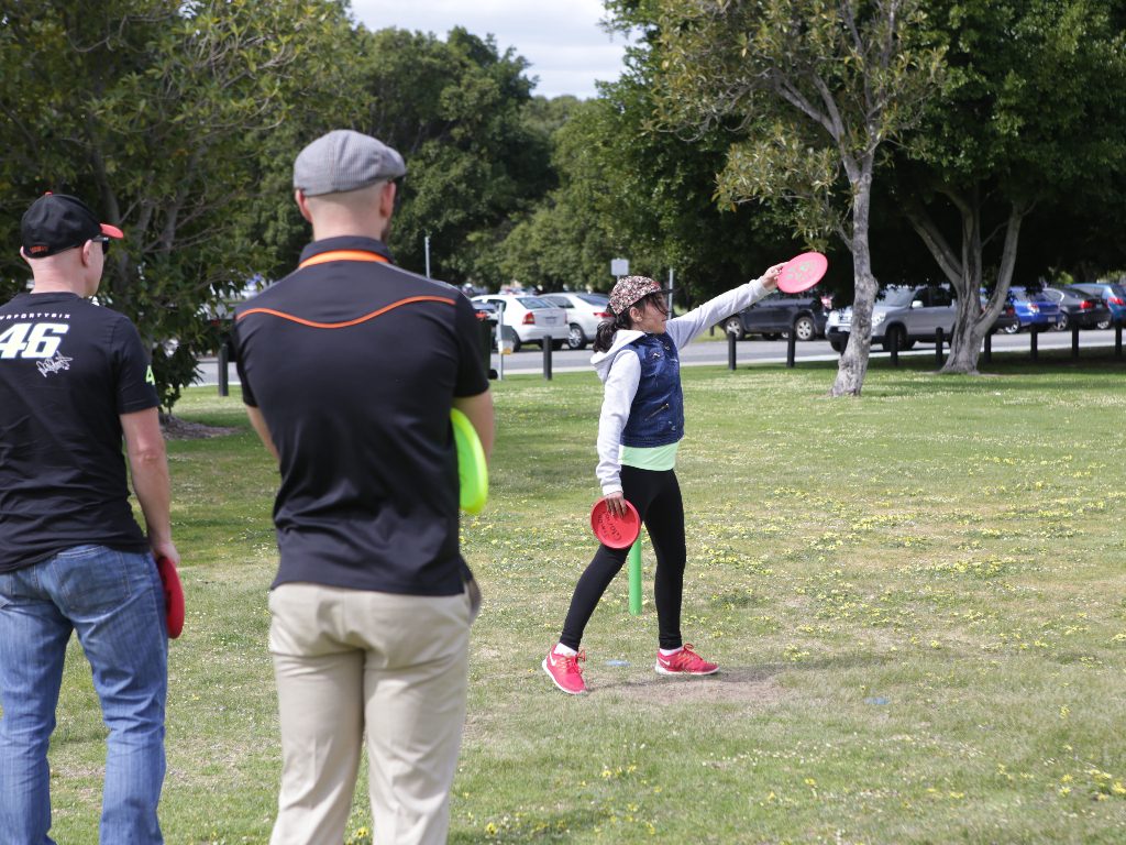 an image of woman playing disc golf while two men watching