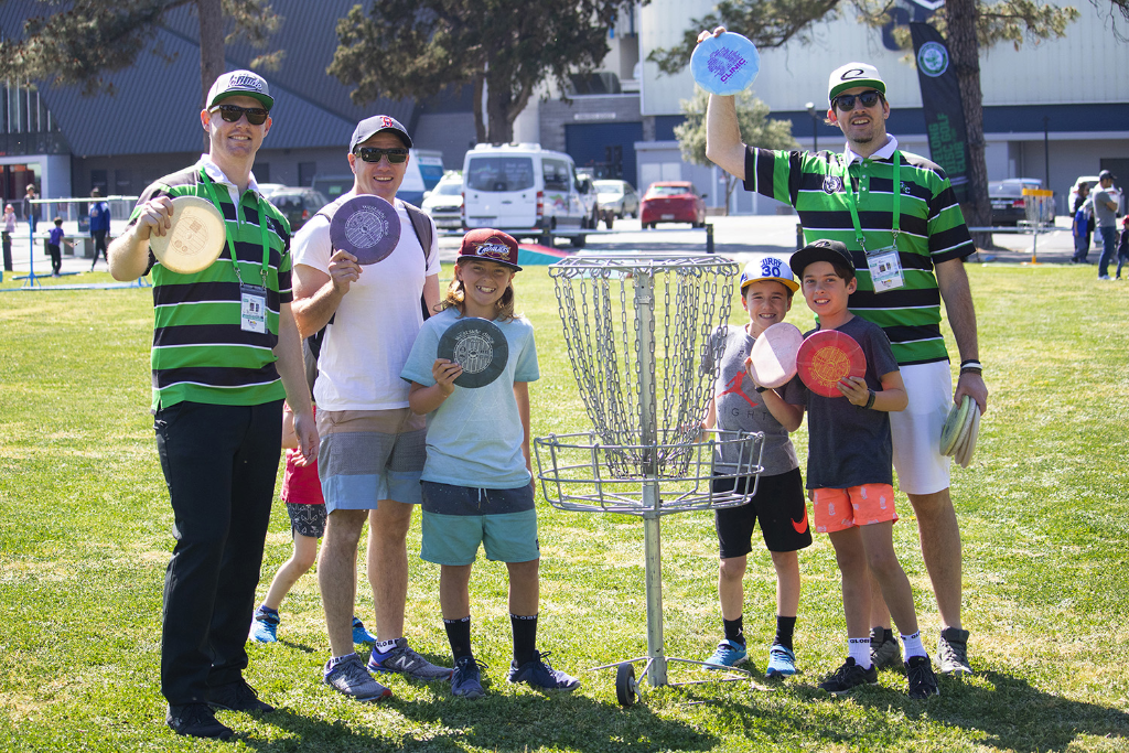 an image of kids and men holding frisbee beside a disc golf basket target